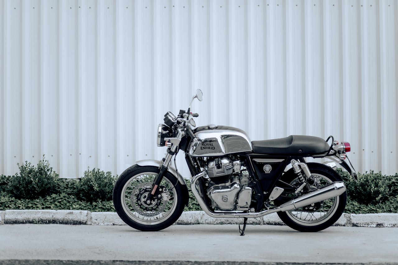 Side view of a Royal Enfield motorcycle parked against a corrugated wall in daylight.